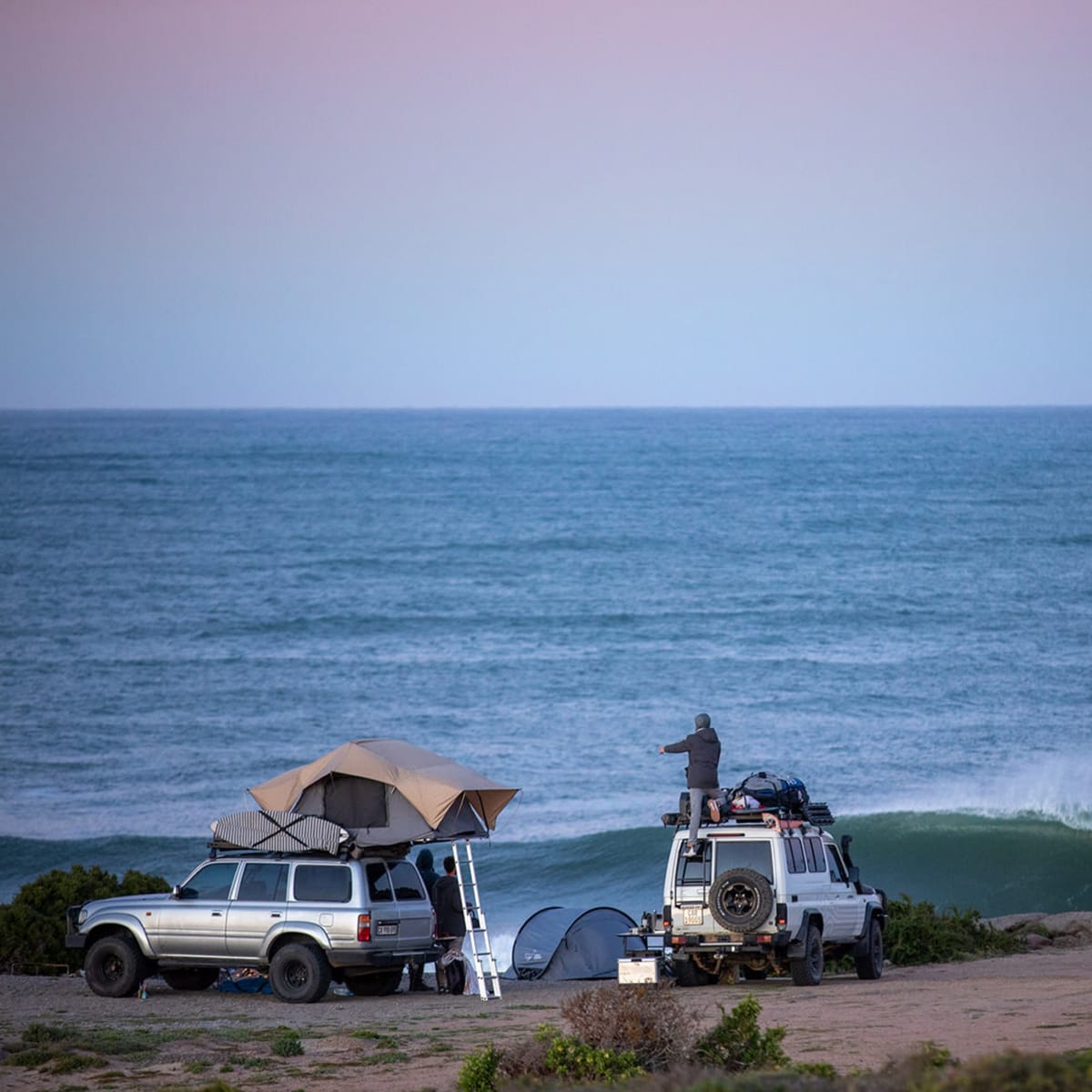 A Land Cruiser 80 and a 70 Series wagon with Front Runner racks camped above the sea