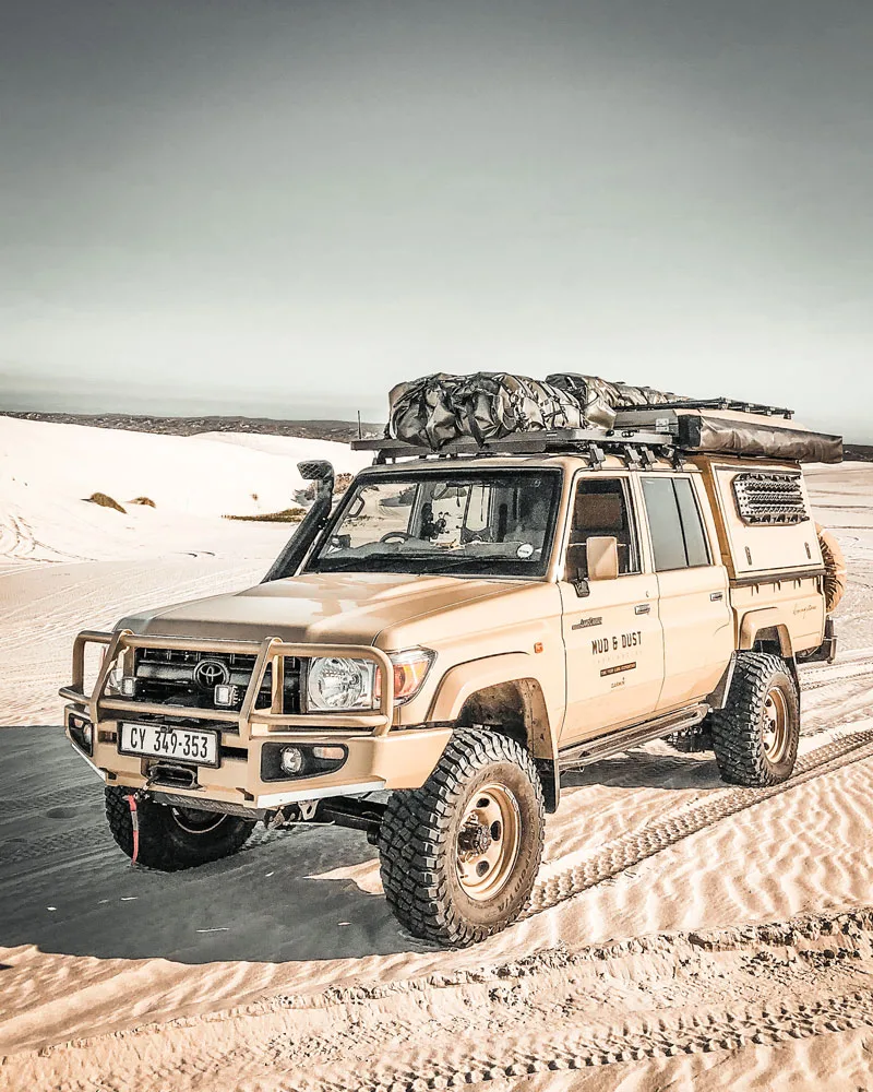 Land Cruiser 79 double cab with canopy and roof rack on white sand dunes