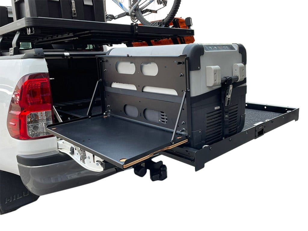 A Dometic fridge on a Front Runner slide pulled out of a Toyota Hilux load bin, with a table folded down off its side