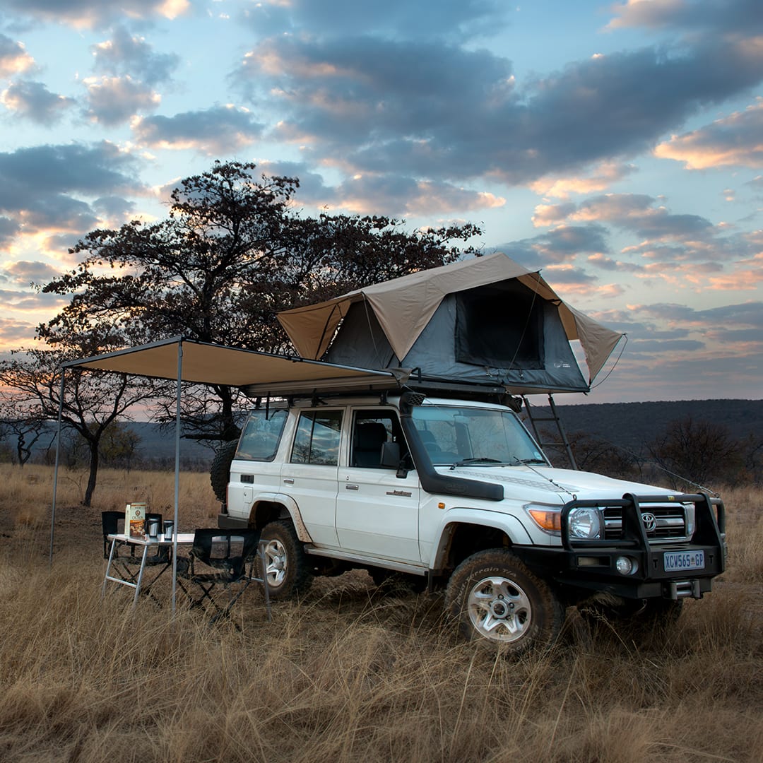 A white 76 Series Land Cruiser station wagon with a rooftop tent and awning, camped in dry bushveld