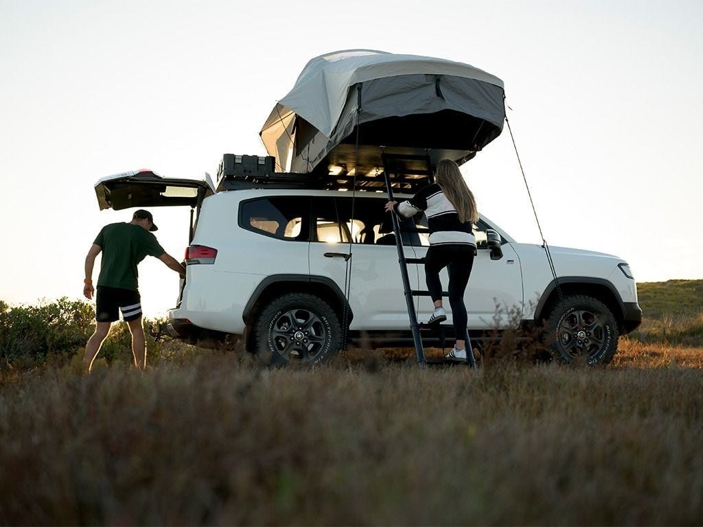 White Land Cruiser 300 with a Front Runner Feather-Lite II rooftop tent open, a woman climbing the ladder