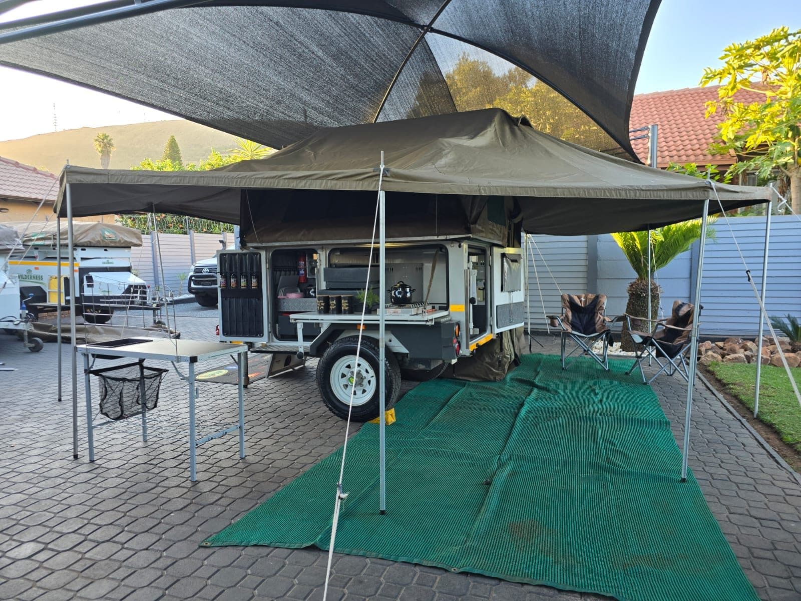 A camper trailer set up with awning, camp table, chairs and ground mat for a shakedown before a trip