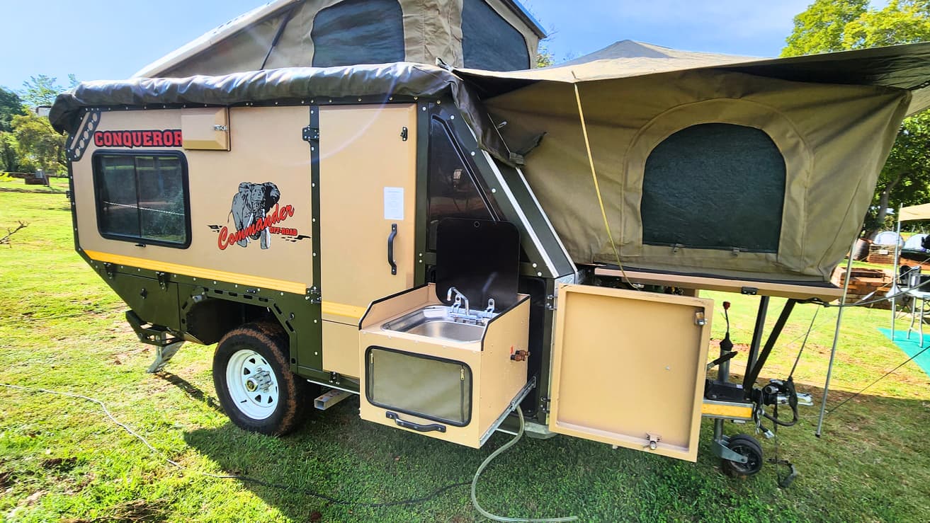 A compact off-road camper trailer with a pop-top tent and slide-out kitchen on a grassy site
