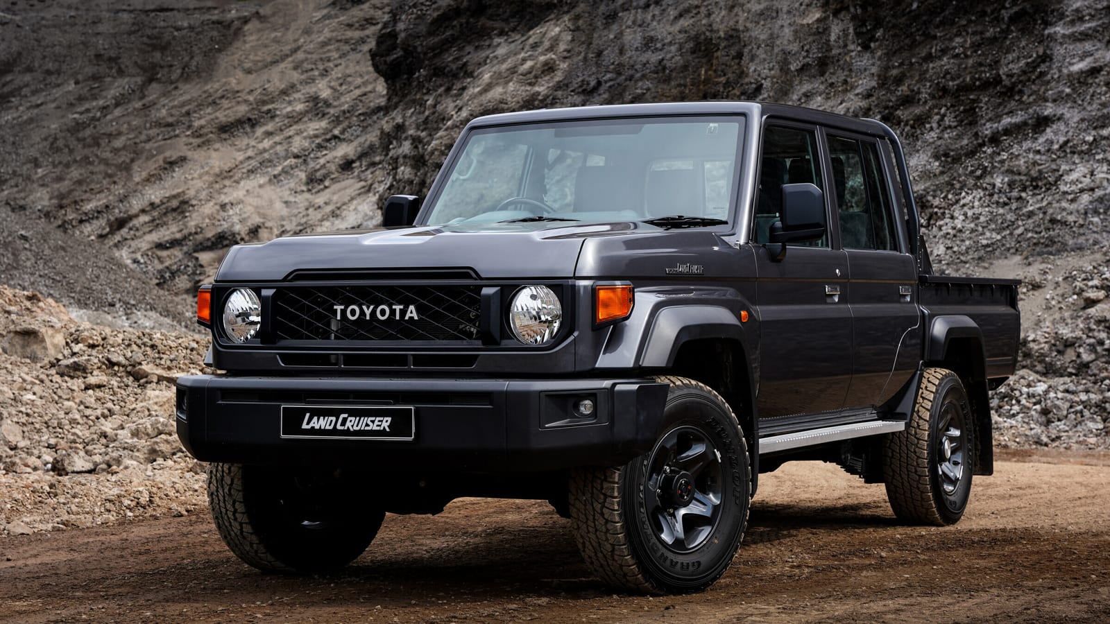 A grey new-shape Land Cruiser 79 double cab on a dirt road, with round headlights and TOYOTA across the grille