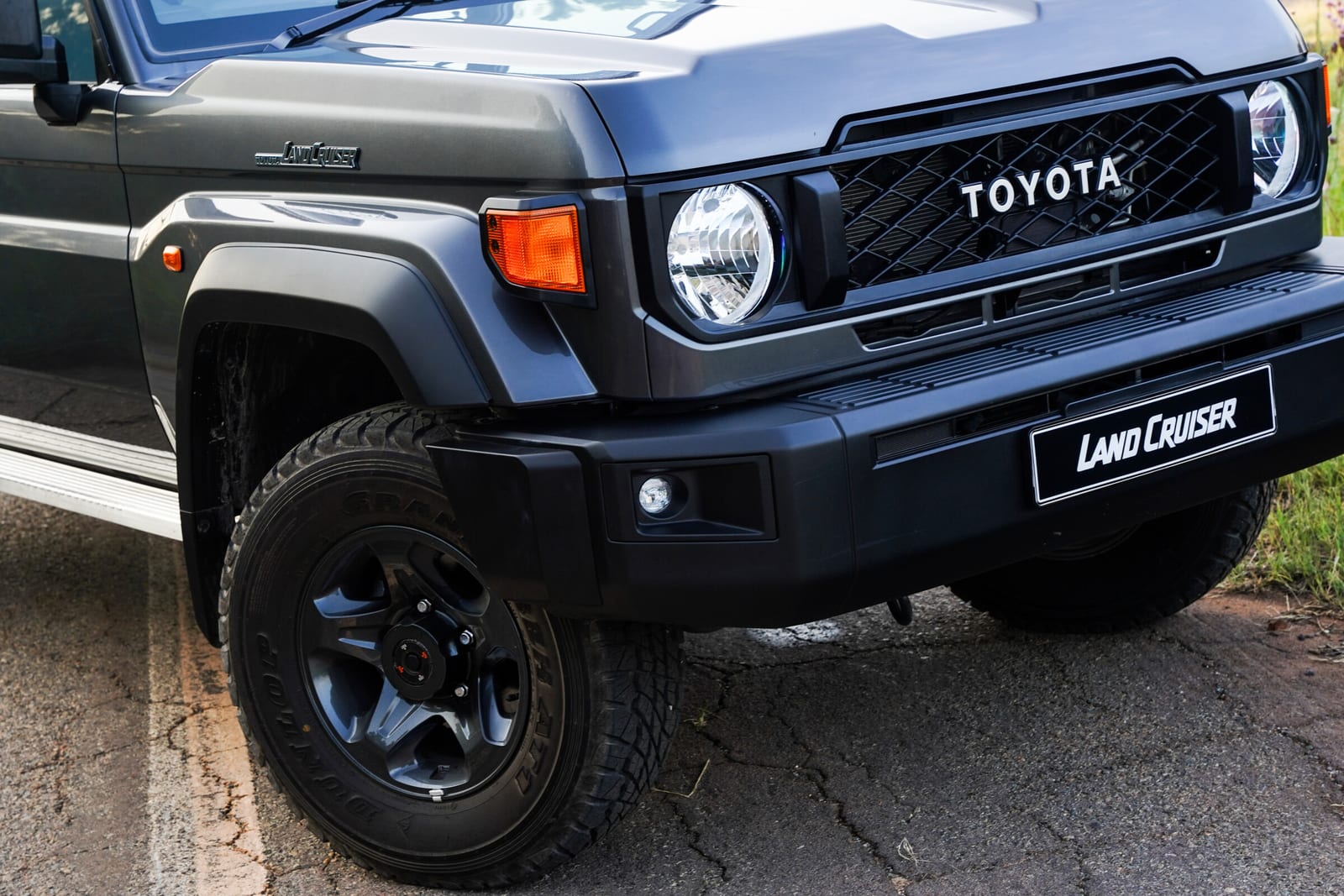 Close-up of the front of a new-shape Land Cruiser 79: round headlight, TOYOTA grille, orange indicator and black bumper