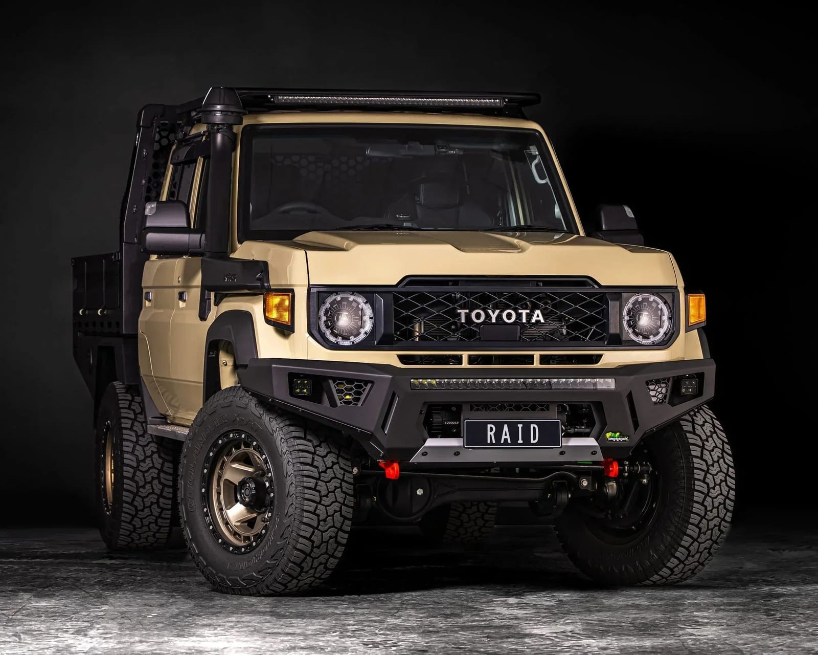 A tan new-shape Land Cruiser 79 single cab in a studio, fitted with a black steel replacement bar with a light bar and red recovery points
