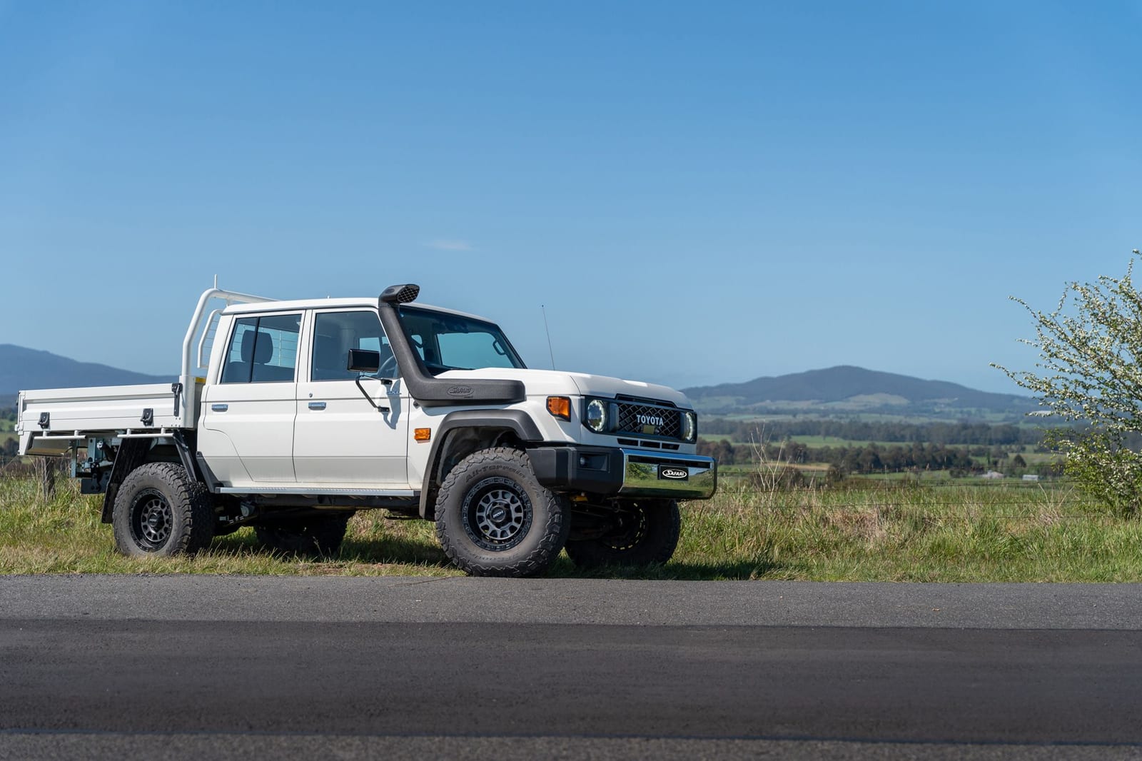 A white new-shape Land Cruiser 79 double cab with a tray and a black snorkel, seen from the side
