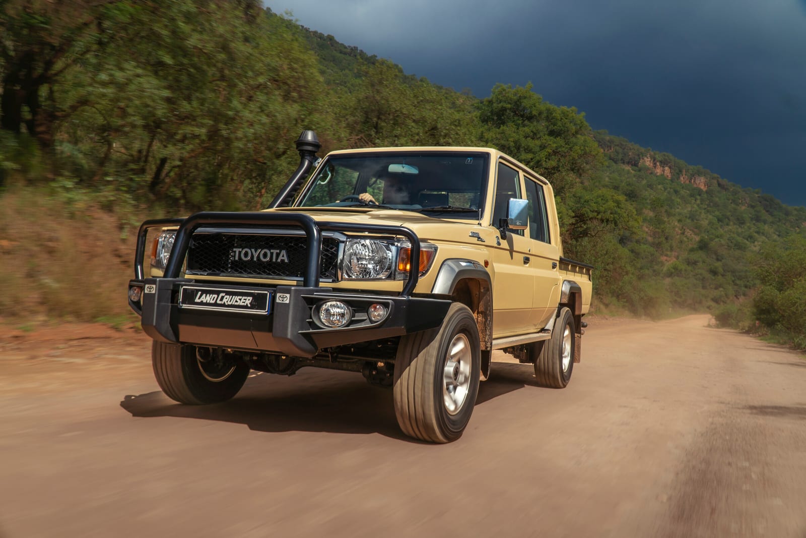 A sand-coloured Toyota Land Cruiser 79 V8 double cab with a snorkel and steel bull bar on a dirt road.