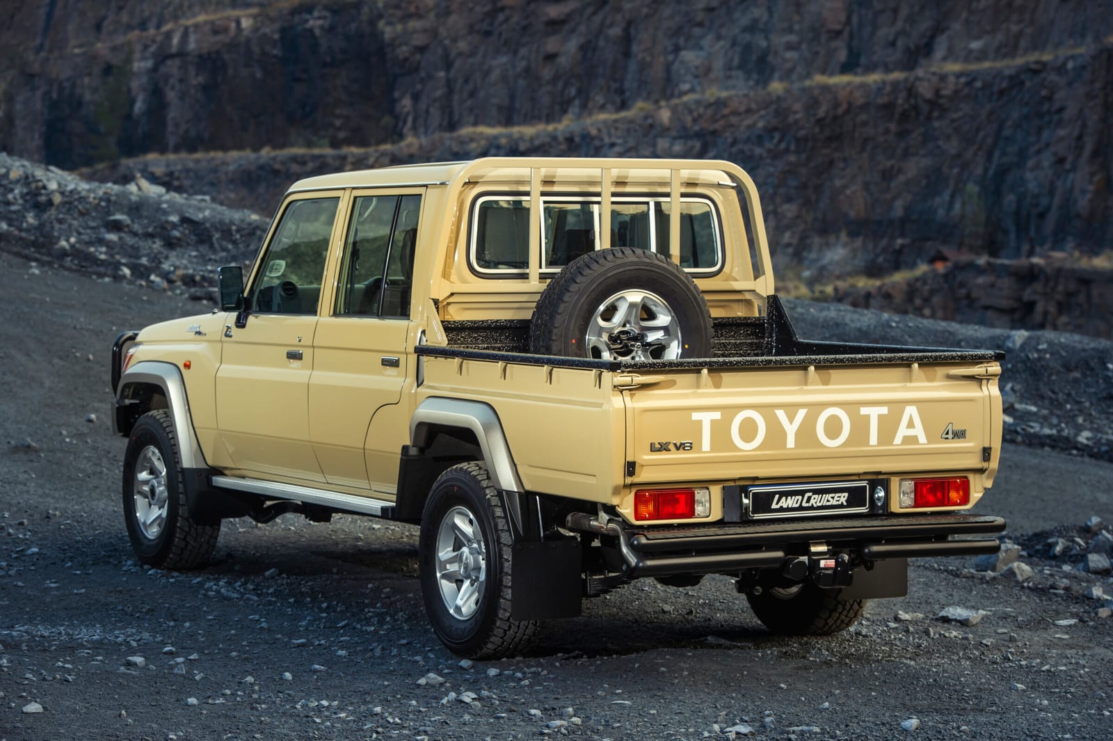 The rear of a sand-coloured Toyota Land Cruiser 79 double cab with the LX V8 badge, spare wheel and towbar.