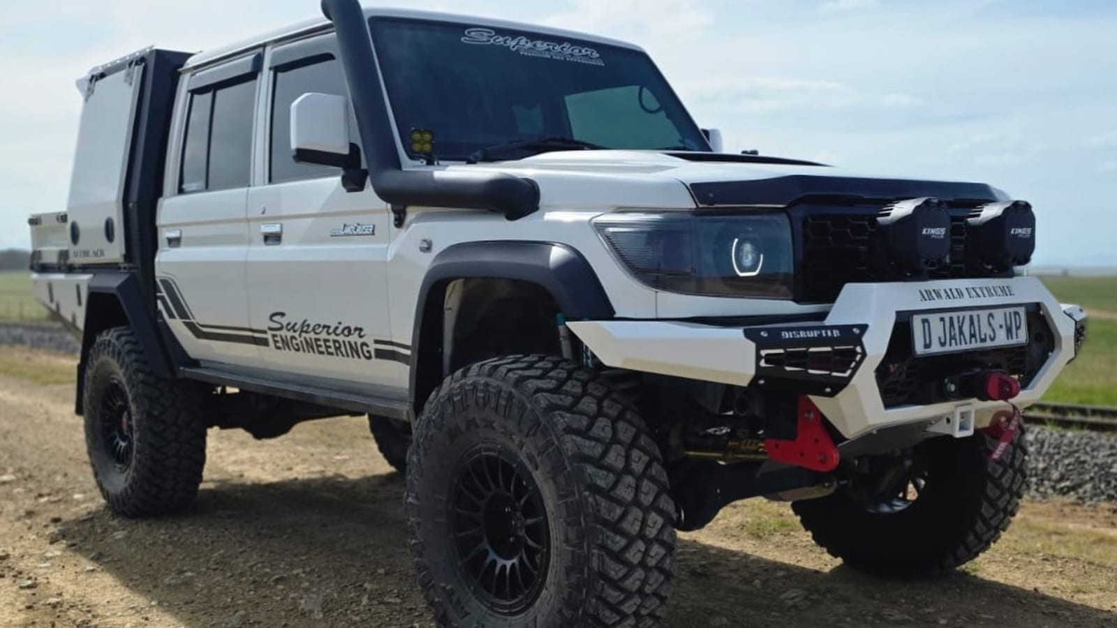 A lifted white new-shape Toyota Land Cruiser 79 double cab on big off-road tyres, on a gravel road, wearing Western Cape plates