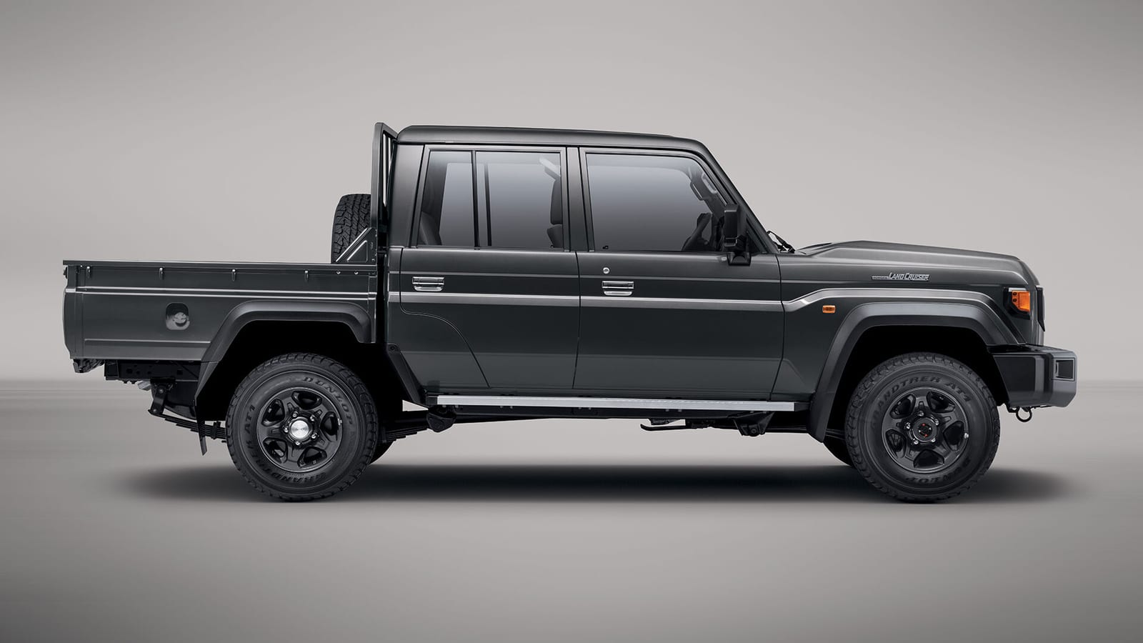 A standard dark grey new-shape Toyota Land Cruiser 79 double cab seen from the side in a studio