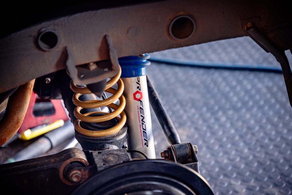 A yellow coil spring and a white Profender shock being fitted at the front of a 4x4 in a workshop