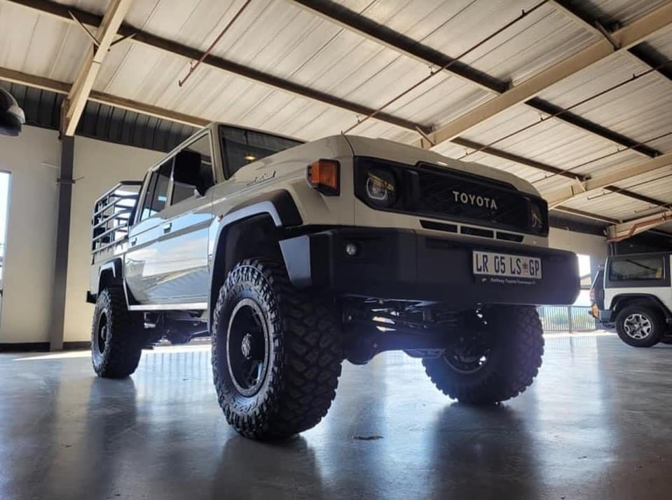 Low-angle view of a kitted sand-coloured Toyota Land Cruiser 79 double cab on chunky mud-terrain tyres and black alloy wheels