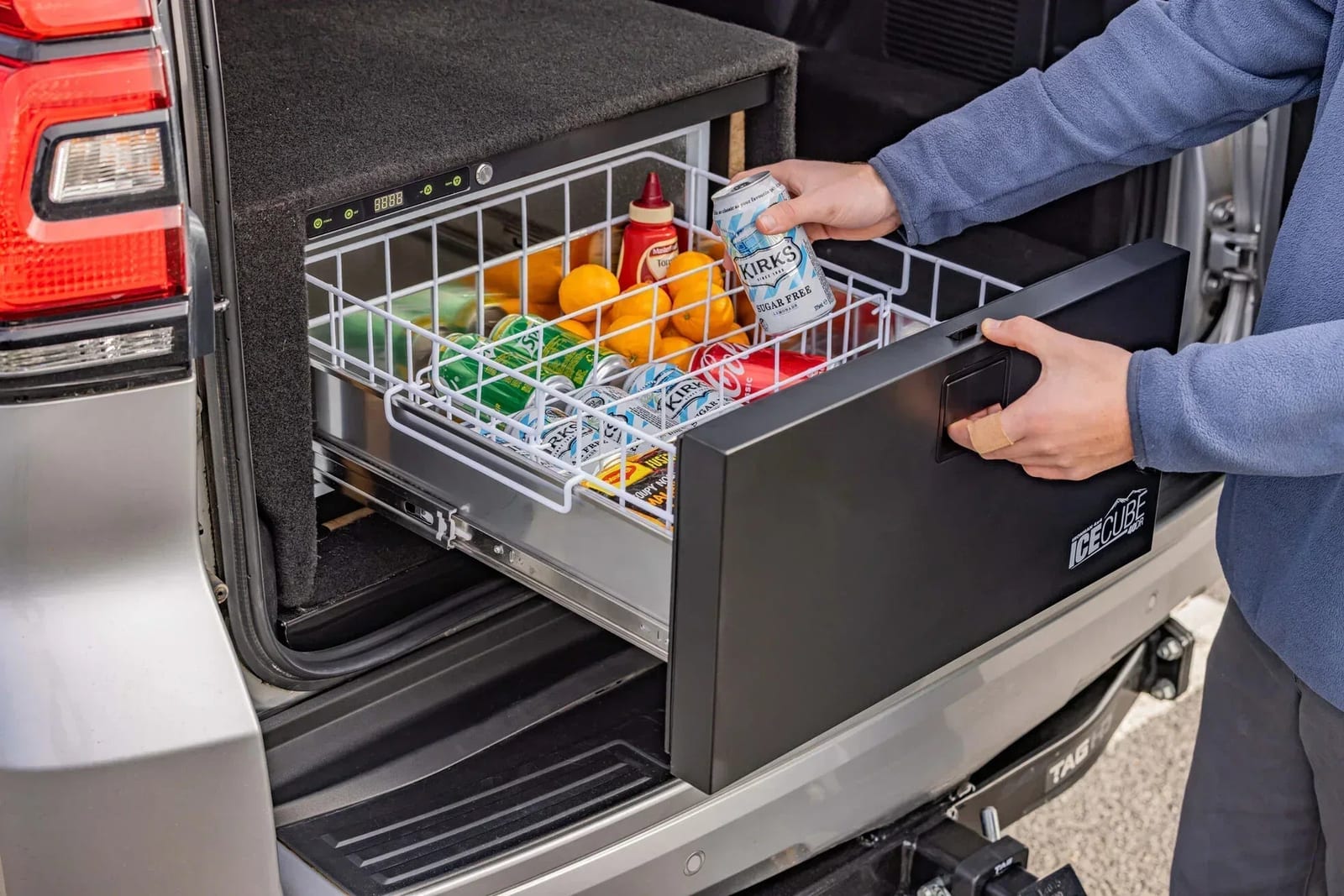 A 40 litre drawer fridge pulled open in the back of a Toyota Prado, full of drinks and fruit