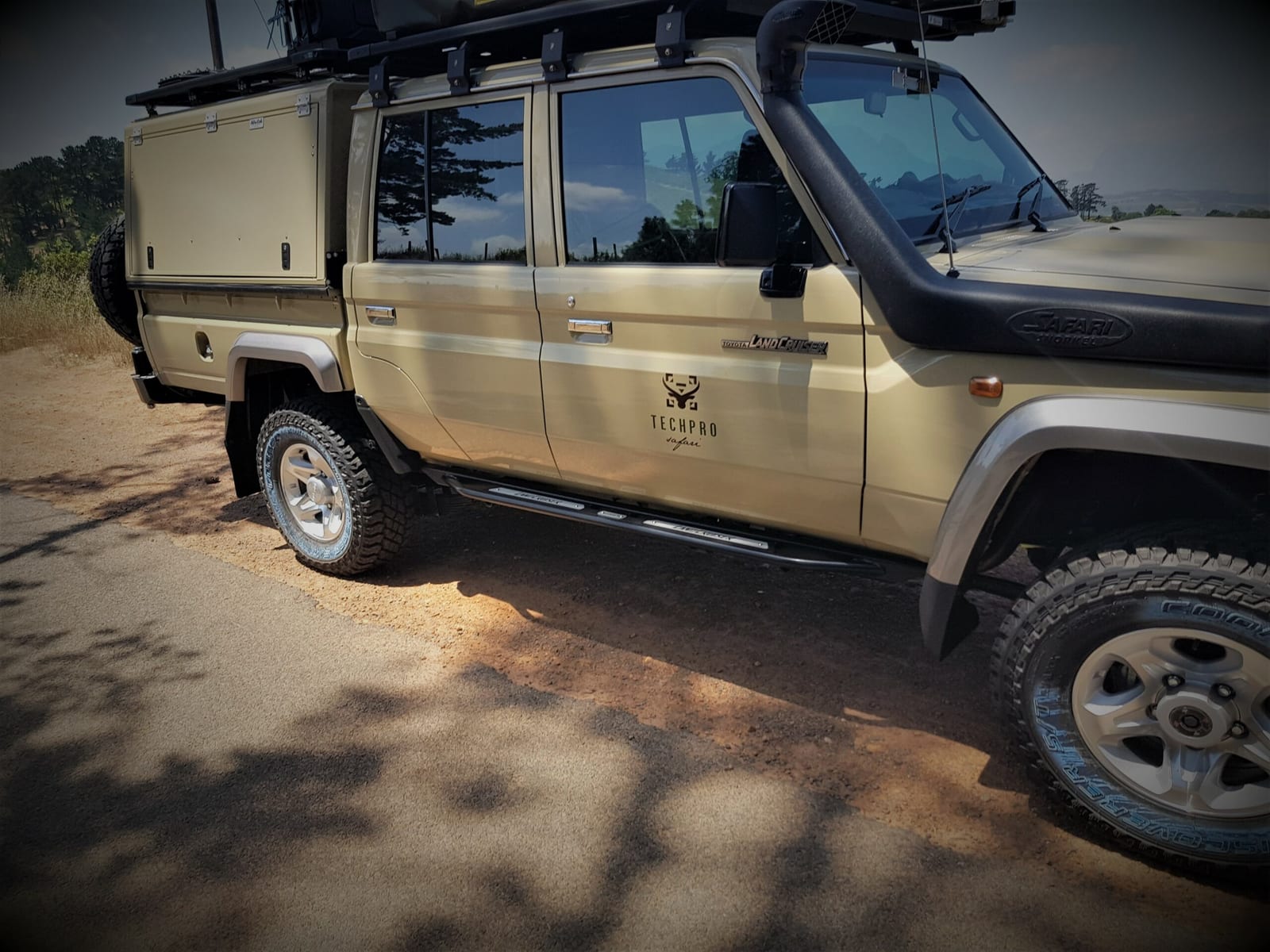 A Land Cruiser 79 double cab with a full canopy, roof rack and snorkel on a gravel road verge
