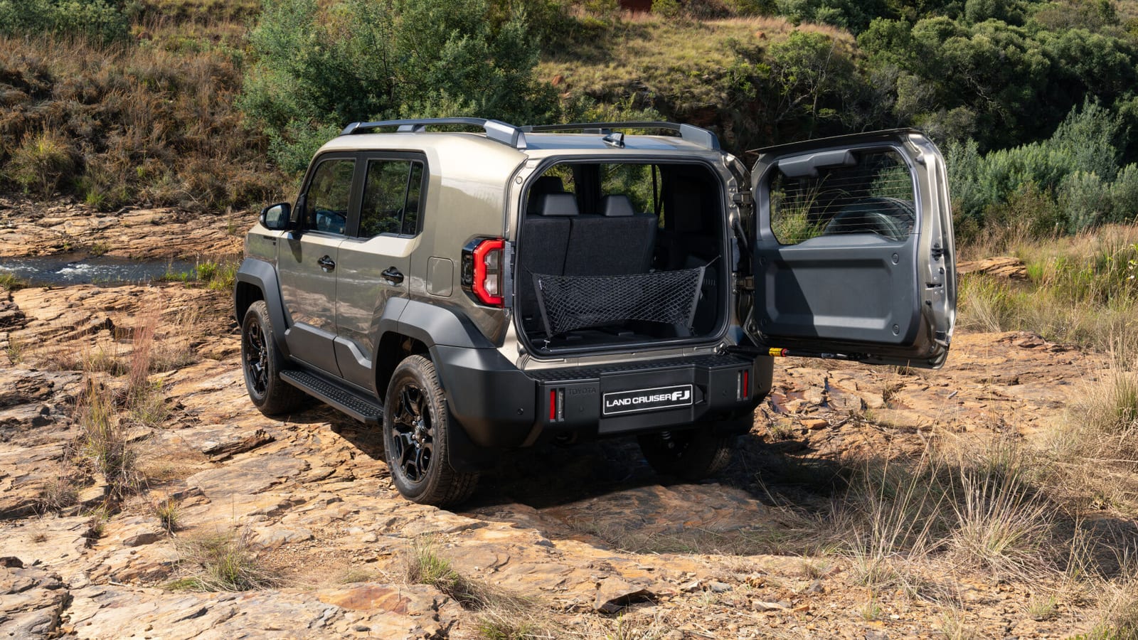 Rear of a Land Cruiser FJ with the side-hinged back door open, parked on rock and fynbos.