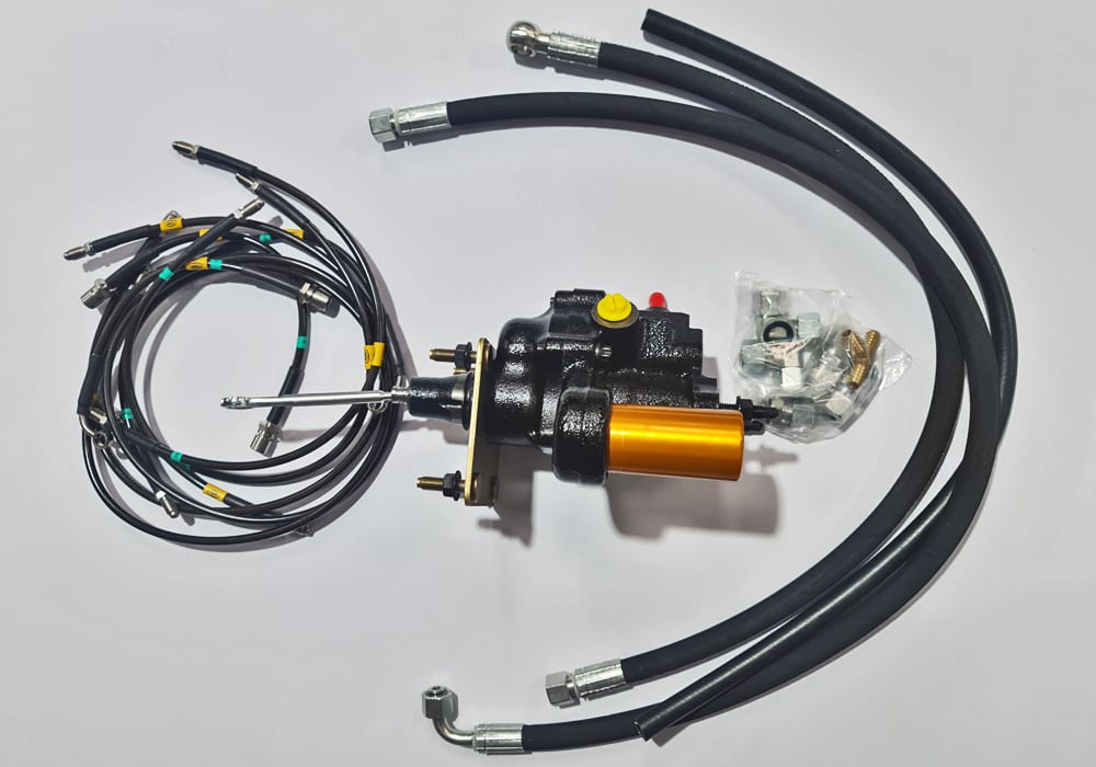 A hydraulic brake booster with an orange canister and a set of black braided brake hoses laid out on a white table