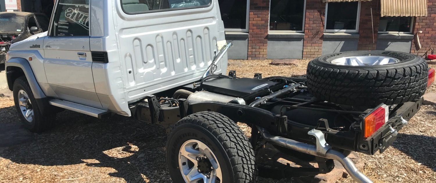 A Land Cruiser 79 single cab with the load bin removed, showing a black extra fuel tank between the chassis rails behind the cab