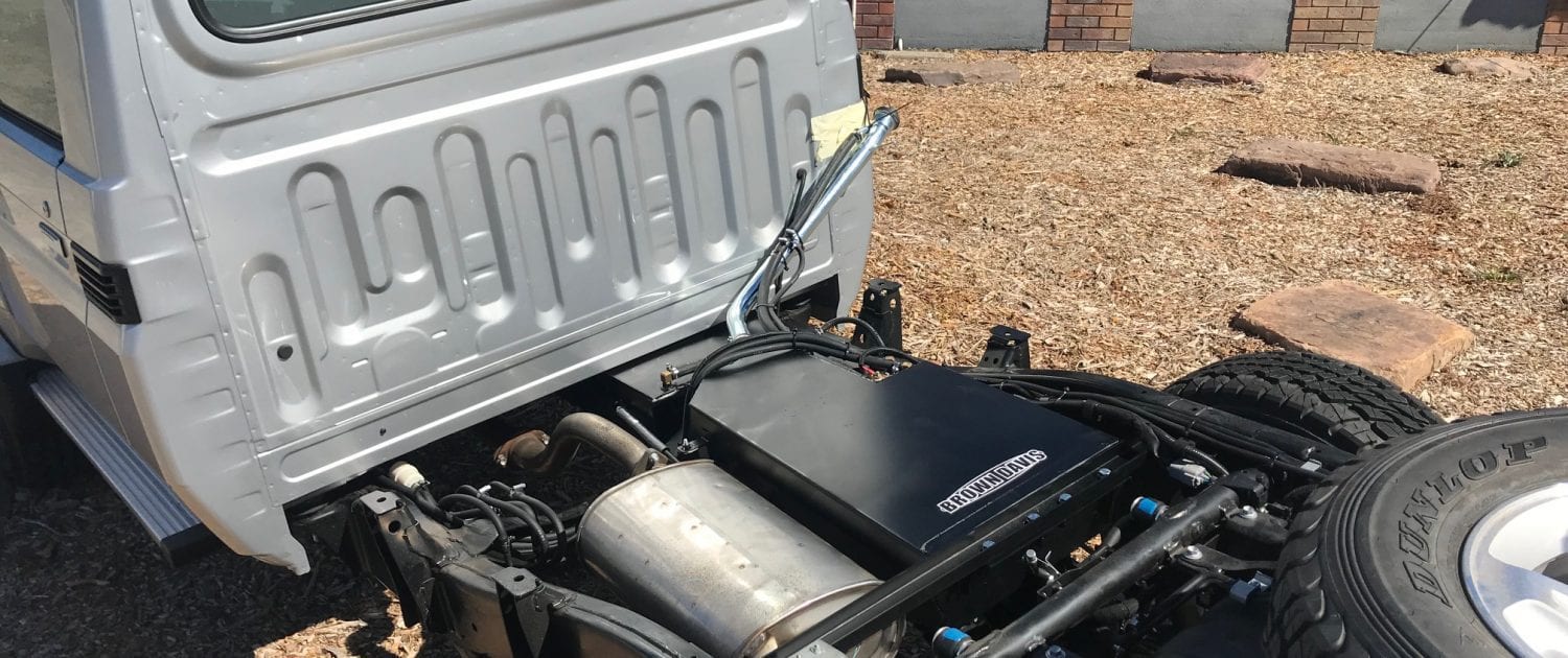 Close-up of an extra fuel tank fitted next to the exhaust silencer under a Land Cruiser 79, with fuel and breather pipes