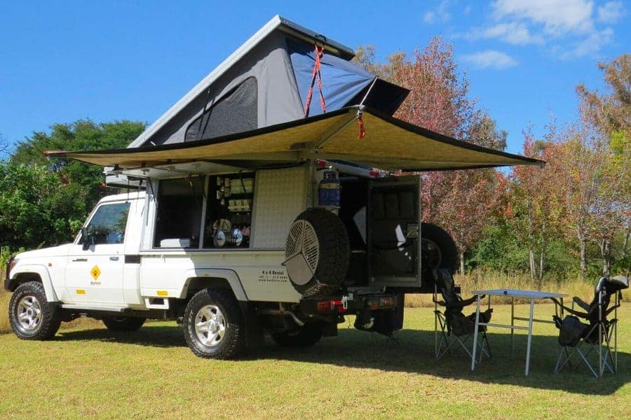 Fully-equipped Land Cruiser 79 rental camper with rooftop tent, awning and camp kitchen set up in the bush
