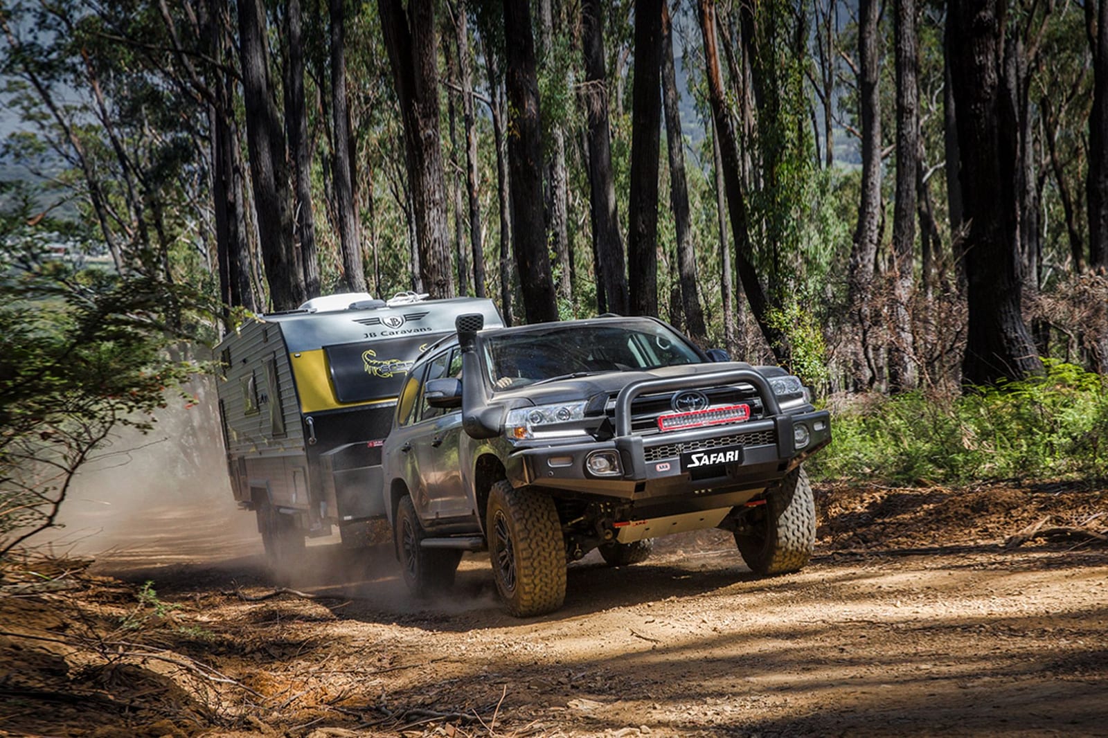 A Land Cruiser 200 Series with a snorkel and a bull bar towing an off-road caravan along a dusty forest track