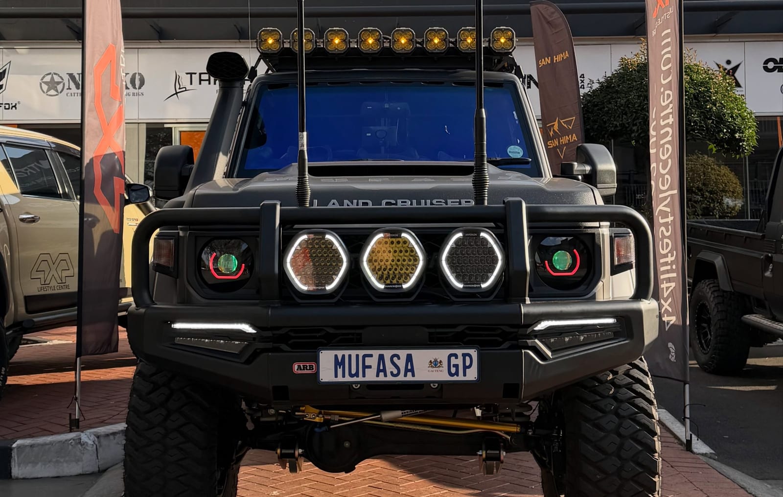 A fully built Land Cruiser 70 Series on Gauteng plates with a snorkel, a steel bar, round spotlights and a roof light bar, parked outside a 4x4 fitment centre