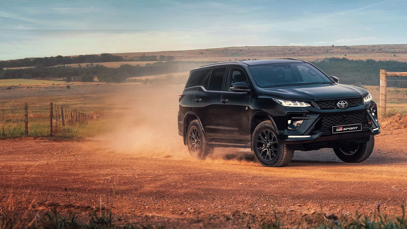 A black Toyota Fortuner driving on a dusty red farm road in South Africa.