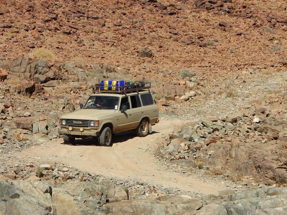 A beige 60 Series Land Cruiser with a loaded roof rack on a rocky track in the Richtersveld.