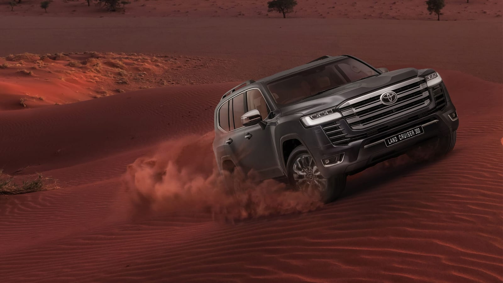 A grey Toyota Land Cruiser 300 driving up a red sand dune.