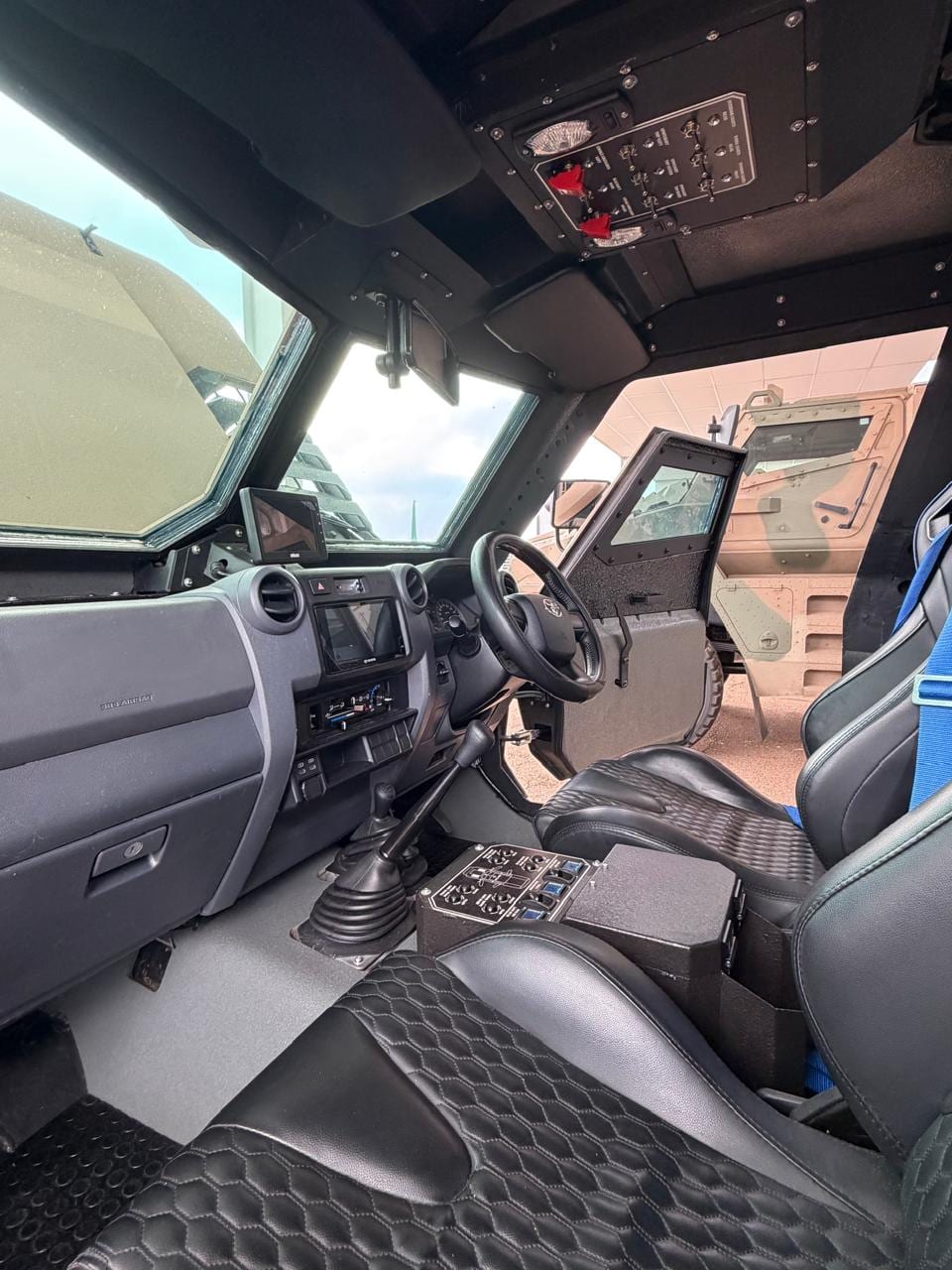 Inside the Milkor Frontier: a Toyota Land Cruiser 79 dash and steering wheel, quilted seats, an overhead switch panel and a thick armoured door