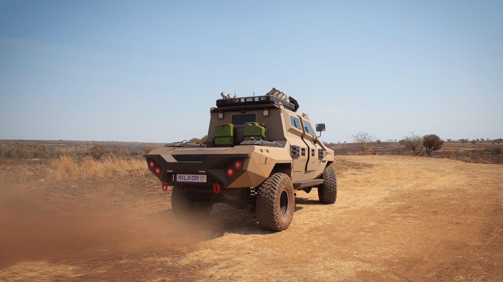 The Milkor Frontier 4x4 from behind, kicking up dust on a dirt road with jerry cans in the load bed
