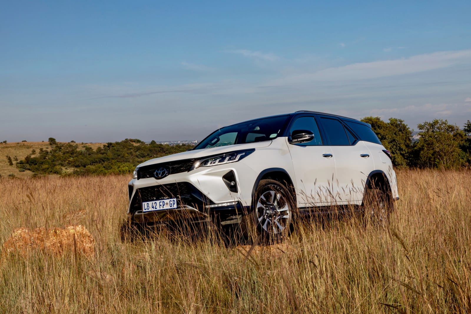 A white Toyota Fortuner with a black roof standing in long grass in the veld.