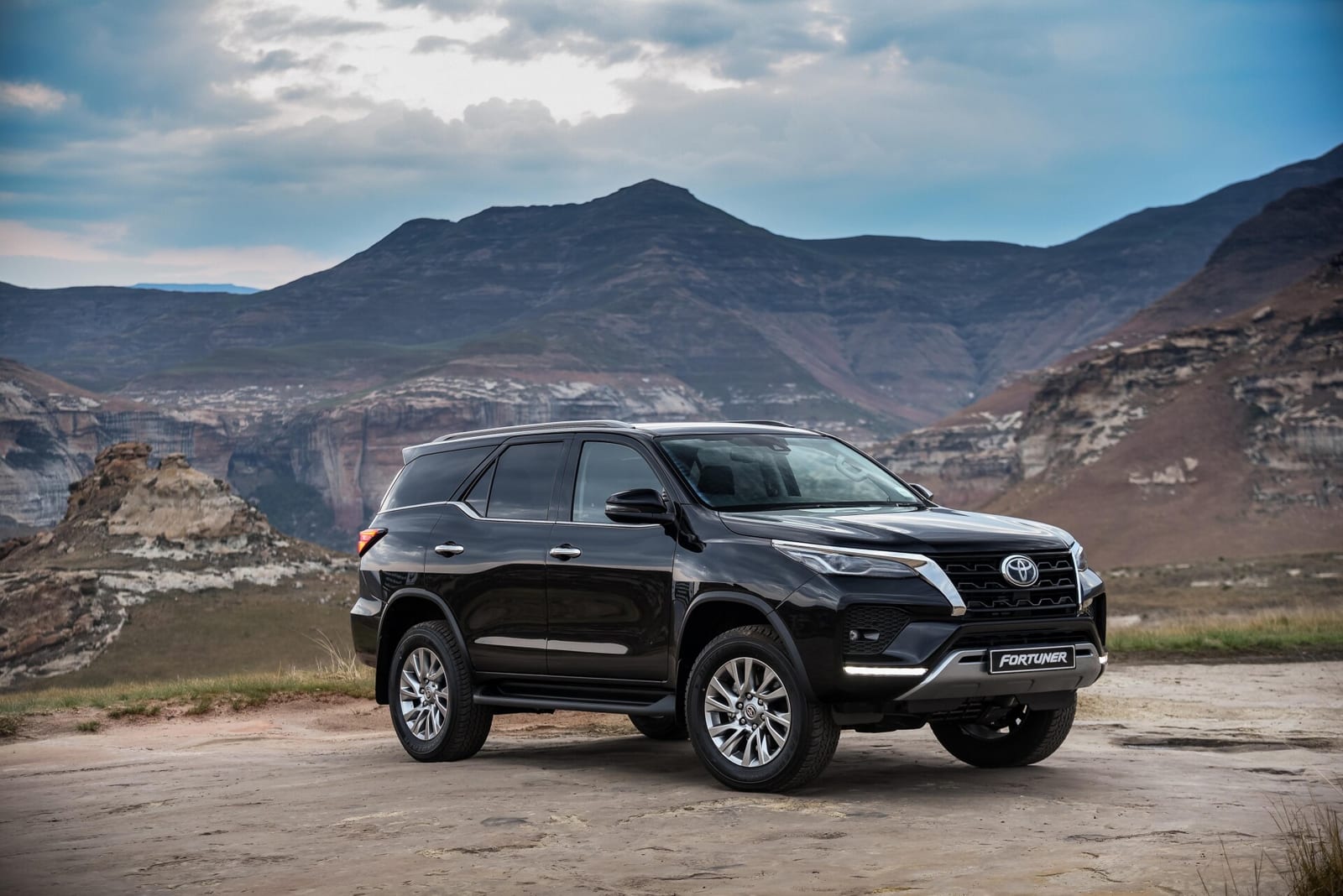A black facelifted Toyota Fortuner parked on rock in front of sandstone cliffs.