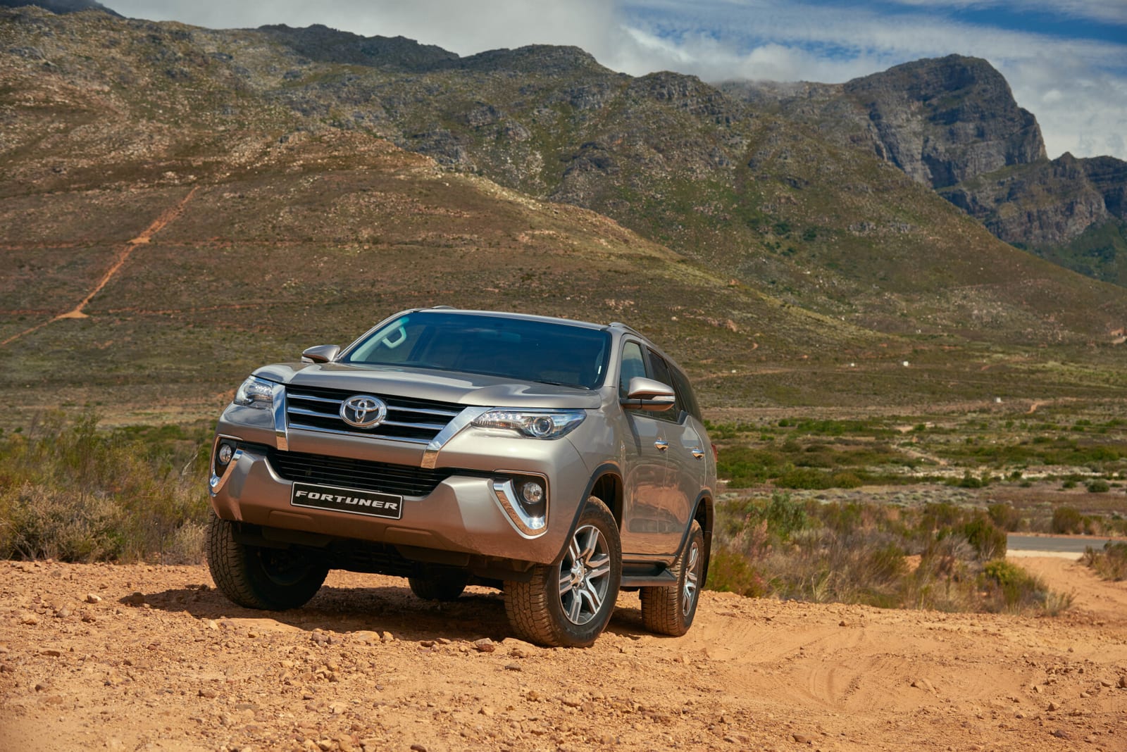 A silver 2016 Toyota Fortuner on a dirt track with mountains behind.