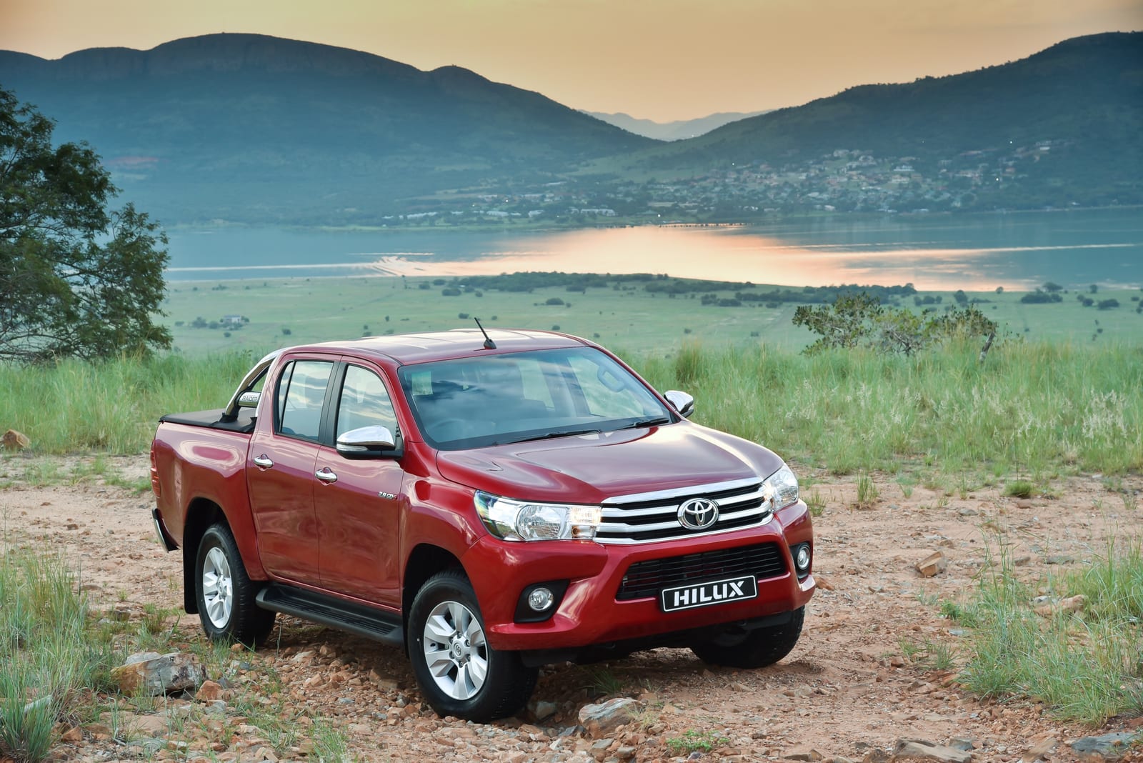 A red 2016-era Toyota Hilux GD-6 double cab parked on a rocky hill above a dam.