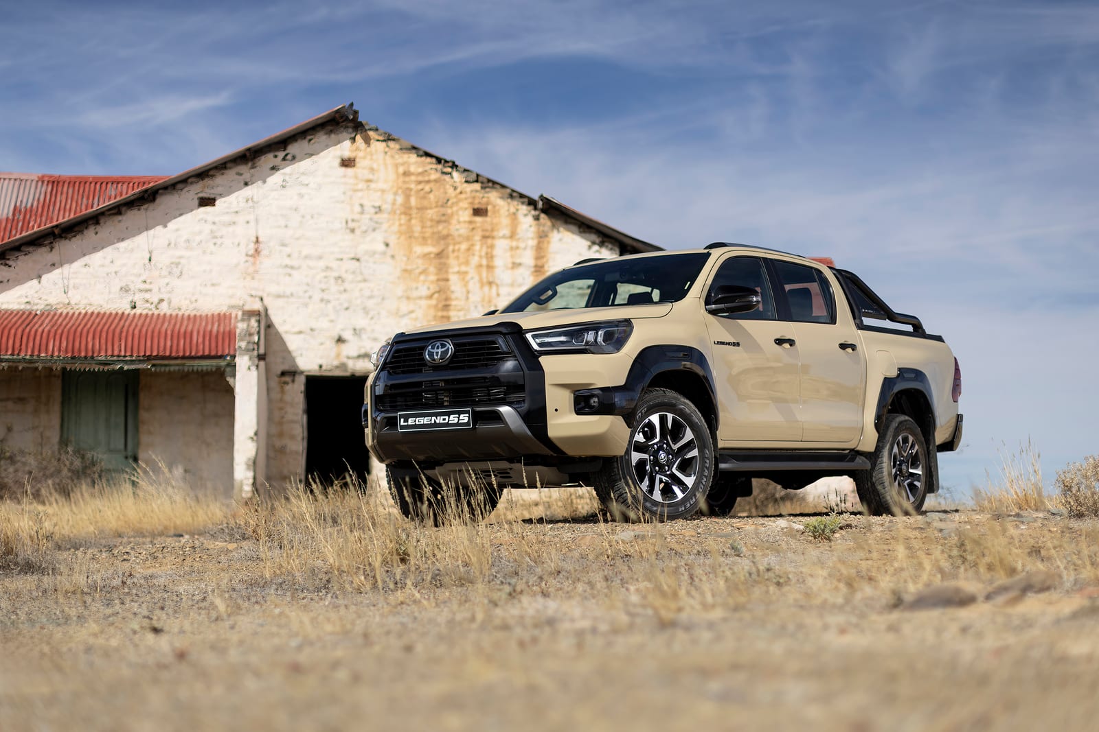 A sand-coloured Toyota Hilux Legend 55 double cab parked in front of an old farmhouse.